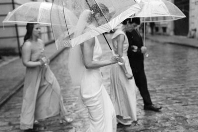 La mariée marche dans la pluie avec son parapluie entourée de sa famille, dans une rue de pierres du vieux-montréal.