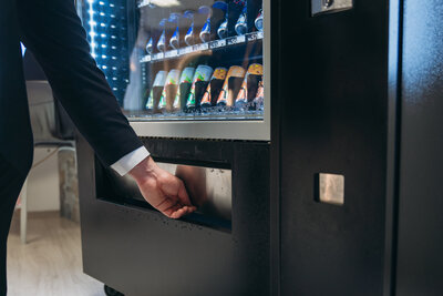 Man in business attire reaching into vending machine to retrieve a bottled drink.