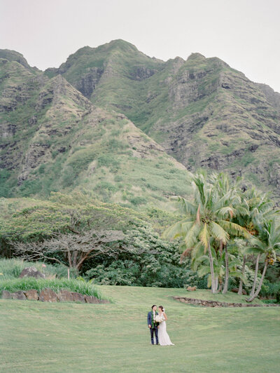 Mai and Daniel stand against the backdrop of Jurassic Park at Kualoa Ranch for their Hawaii wedding.