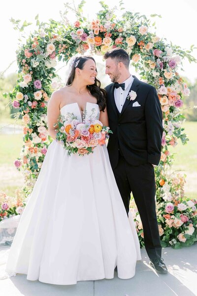 Bride and groom smiling outdoors with whimsical garden-style bouquet