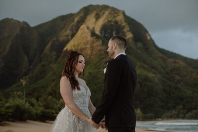 Bride and groom stand holding hands on beach