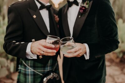 Two grooms clink cocktail glasses at wedding