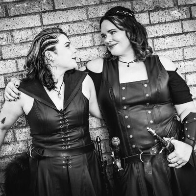 Black and white photo of two brides in leather dresses with swords and braided hair at a Renaissance-themed Las Vegas wedding.