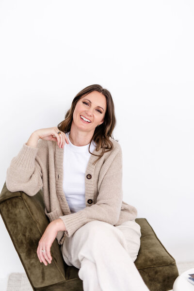 woman standing against white background with travel magazine in hand,  smiling and wearing a casual white button down and jeans.