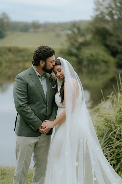 A natural and unposed wedding portrait of a bride and groom holding hands as he kisses her forehead after their Bellingen elopement  at the converted church in Fenrmount