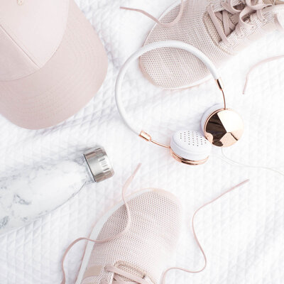 collection of workout gear including pink cap, pink shoes, white and gold headphones, white water bottle, and white towel