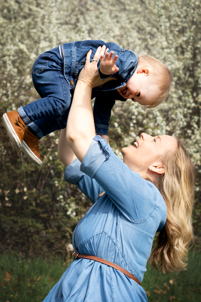 Mother holds son above her head as they play in front of Spring blossom