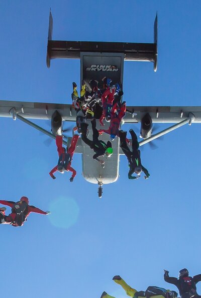 Eine Pink Skyvan fliegt durch den strahlend blauen Himmel. Das Bild zeigt eine Gruppe Fallschirmspringer, die gerade aus dem Flugzeug springt