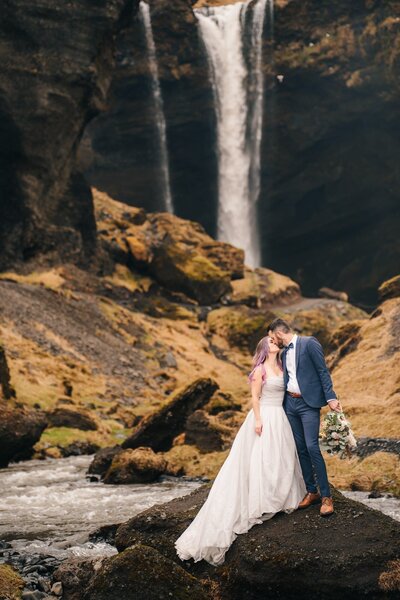 A couple sharing a kiss against a beautiful Icelandic waterfall as the backdrop during their elopement.