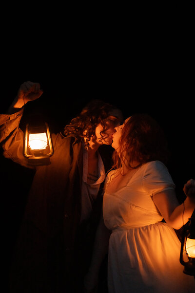 Two people kissing in darkness while holding up lanterns