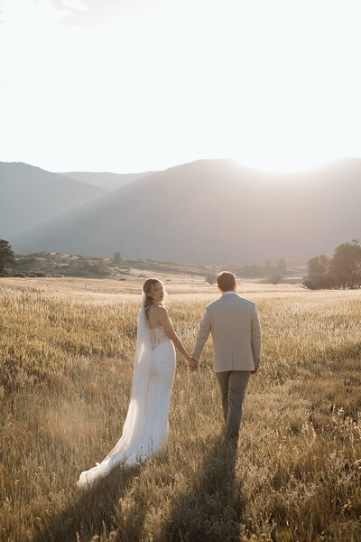 bride and groom walk into the sunset holding hands in a field in Colorado