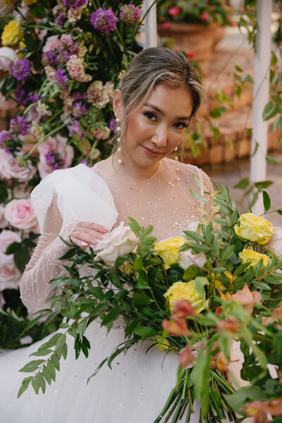 bride on wecding day with vibrant florals under floral arch