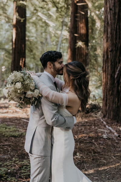 Bride and Groom holding each other close with foreheads touching and bride touching groom's chest in a field surrounded by trees by Big Sur Elopement Photographer Kasey Mantiply
