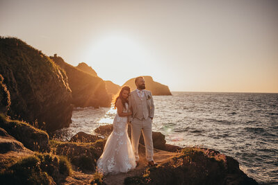 bride and groom look out to sea during sunset
