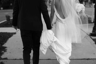 bride and groom walking together while groom holds up bride's wedding dress.