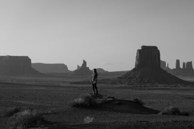 Brisa stands on rock in black and white at Monument Valley vista.

