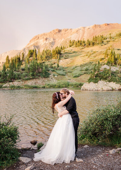 A couple embraces at sunrise next to an alpine lake in Buena Vista