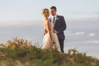 Groom looking at bride while on beach dune after wedding in Cancun