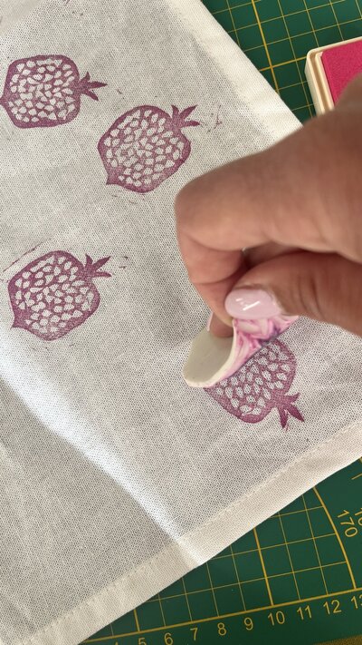 Blockprinten van eigengemaakte granaatappel stempel met roze inkt op een servet tijdens een workshop.