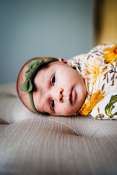 baby swaddled in flower blanket wearing a green headband