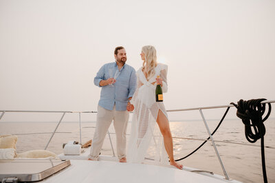 The couple is looking ta each other standing on the deck of a yacht holding drinks - Shot by Wedding Photographers in Toronto