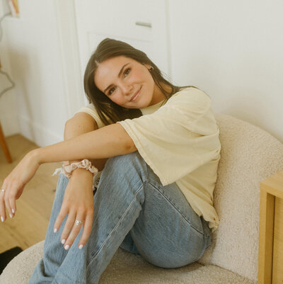 Alexandra Eveland in a yellow t-shirt and blue jeans sitting in a chair and smiling softly