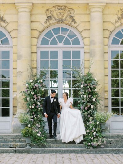 bride and groom walking together in front of big windows