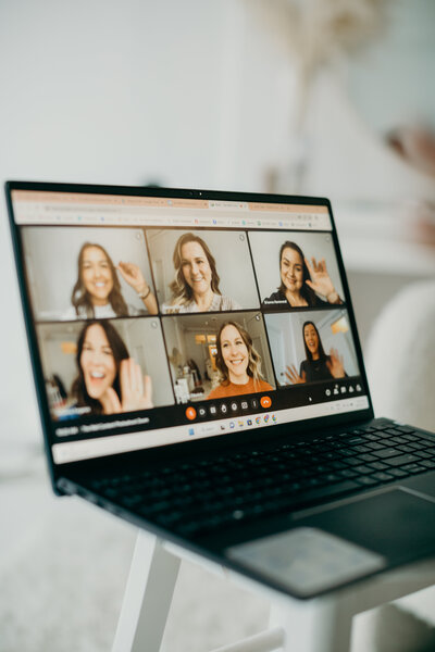 A close up of a laptop while on a video conference call with six women's faces .