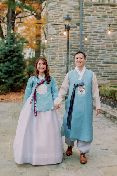 A wedding couple smiling as they hold hands and walk along a stone path 
