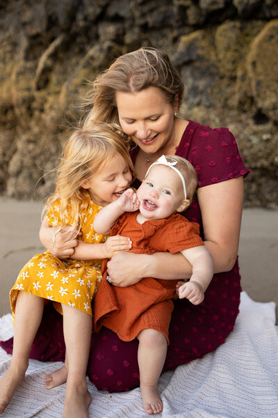 A mother holding two young daughters on her lap while being photographed by a Portland Oregon family photographer.