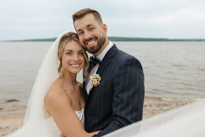 bride and groom sitting on rocks with Lake superior in the background and tall, green, pine trees