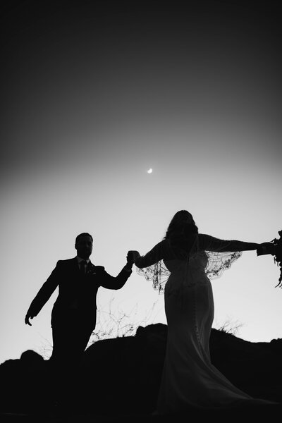 Black and white photo of bride and groom dancing in desert at night