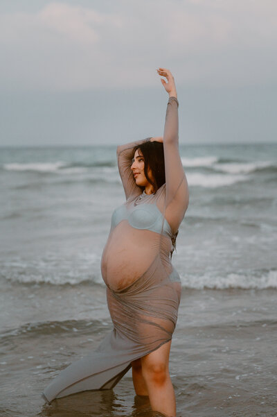 Pregnant woman posing at the beach in flowy dress during sunset lifestyle maternity shoot in Florida