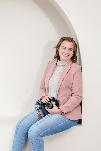 Kansas City family photographer sitting in an archway, holding her camera and smiling.