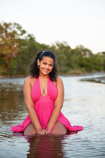 High school senior photography in Wichita, KS beautiful senior girl sitting in water in pink maxi dress