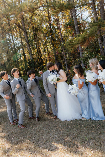 Bride and groom laughing with wedding party in pale blue dresses and gray suits during a joyful outdoor ceremony in Alabama — EC Photography