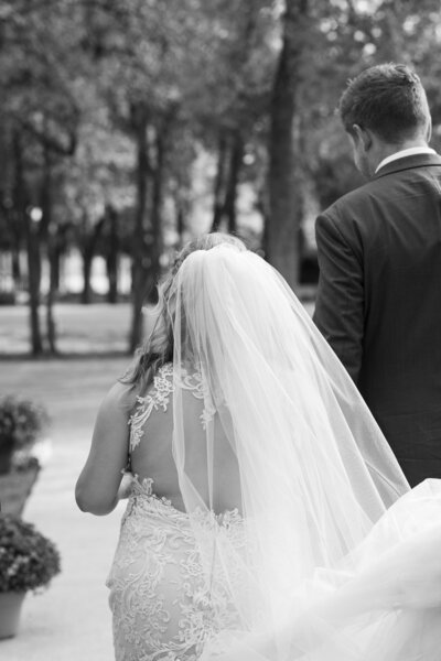 Austin-based wedding photographer captures a beautiful black and white photo of a bride and groom walking down a path.