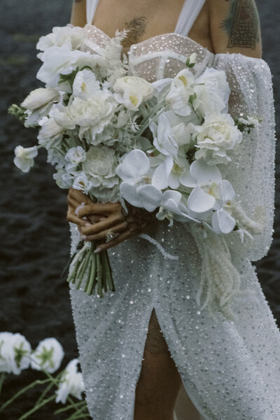 bride with a sequin dress holding a big bouquet of white flowers on a black sand beach in iceland