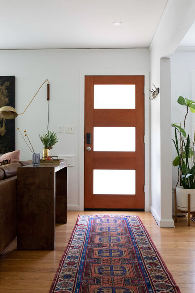 An entryway featuring a door, decorative rug and houseplants representing an example of organic modern interior design.