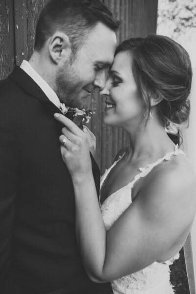 Black and white photo of bride pulling on grooms suit while smiling nose to nose by Iowa City wedding photographer Sabrina Wilham