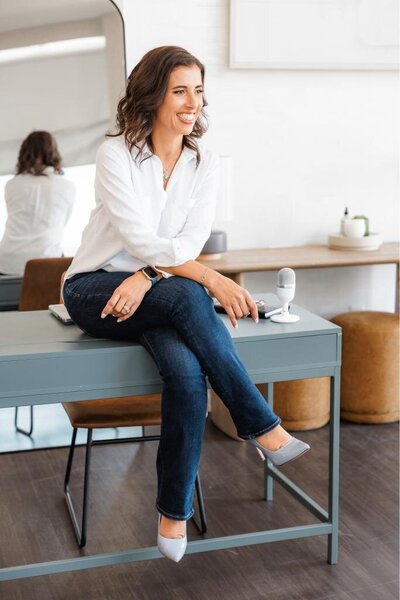 Jo, the founder of Branding by Jo Sitting on a desk in a studio in Orlando smiling to the side during a brand photo session.