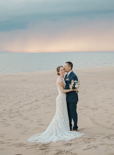 A couple kisses on the beach at sunset at their wedding in Ludington, Michigan