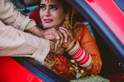 Sikh bride holding hands with her father in the window of the car before they drive off after her doli vidai