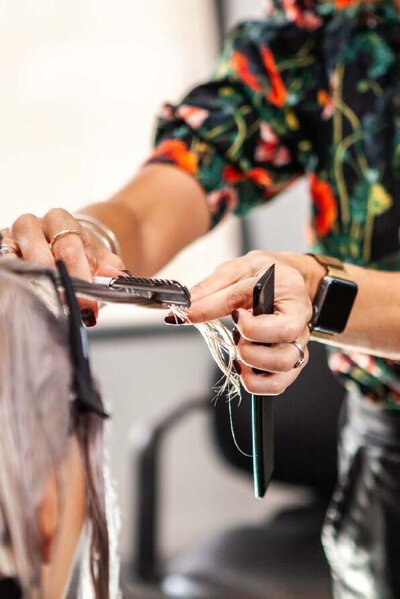 Close-up of a Katy Reeve Hair stylist using a flat iron to create precise haircuts on blonde strands.