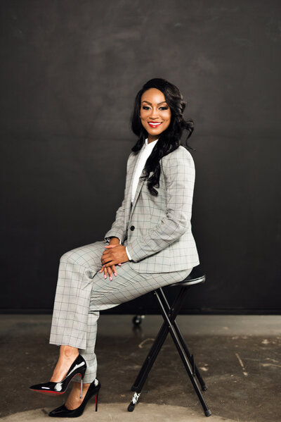 Professional headshot photo, woman in a grey suit sits on a chair in a photography studio.