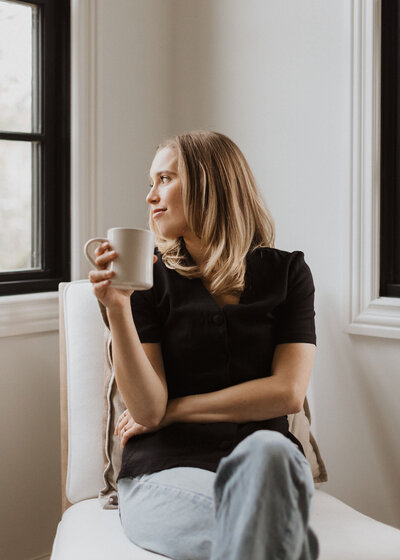 woman at chair looking out window with mug