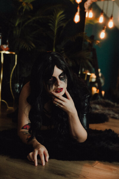 Woman with dark makeup and long black hair lays on a fur rug during a dramatic conceptual portrait session in Jacksonville, Florida.