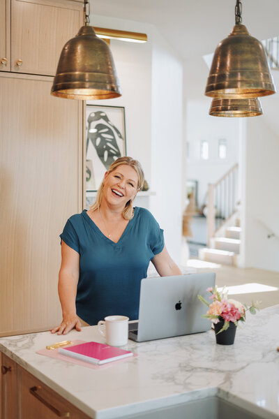 Business coach Melanie Greenough wearing a blue shirt standing by a laptop