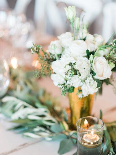 Wedding centerpiece with white flowers and greenery in a gold vase with garlands and candles