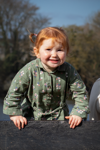 Toddler grins at the camera whilst standing on a bench